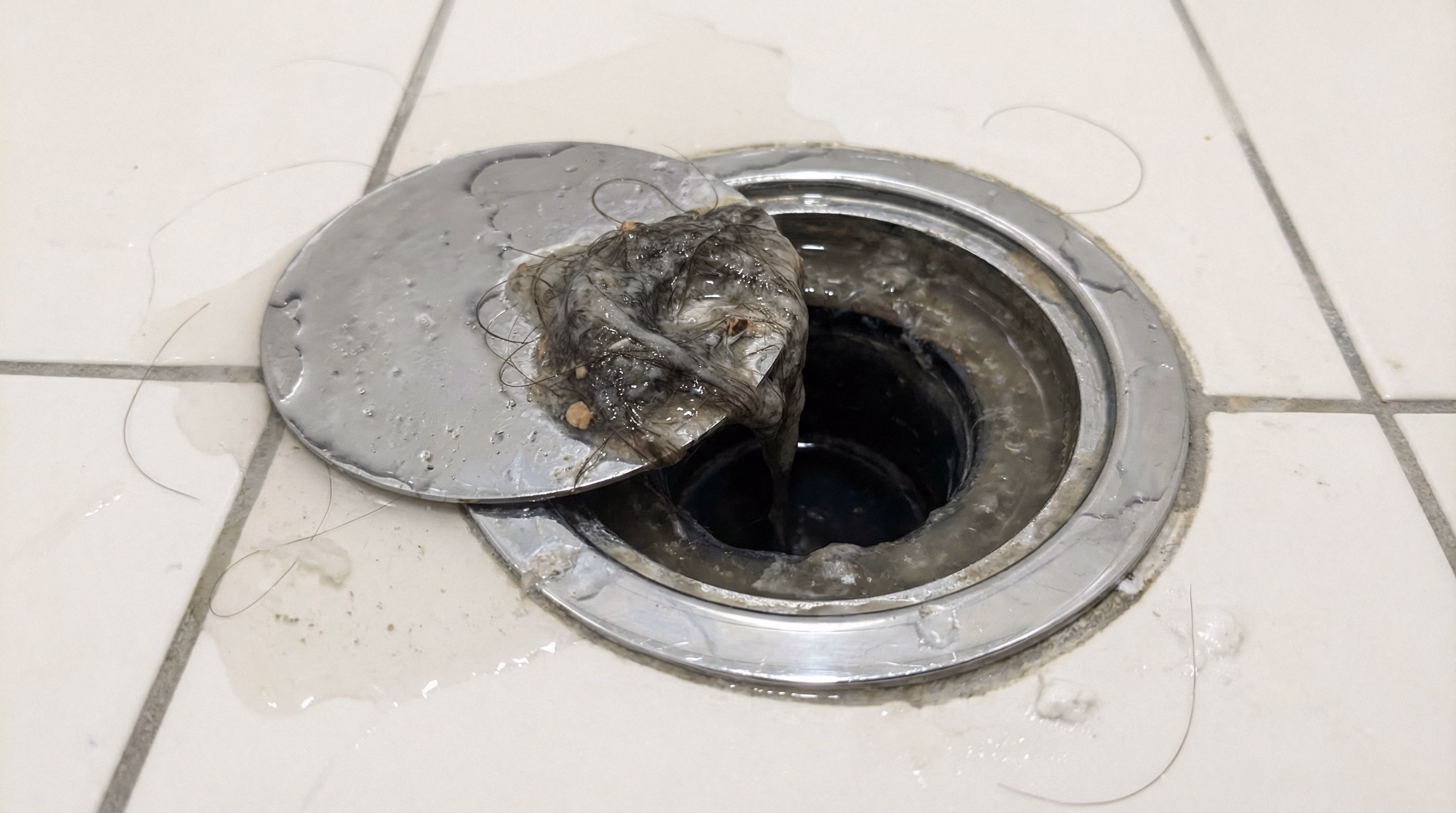 Ralo de banheiro entupido com acúmulo de cabelos e resíduos